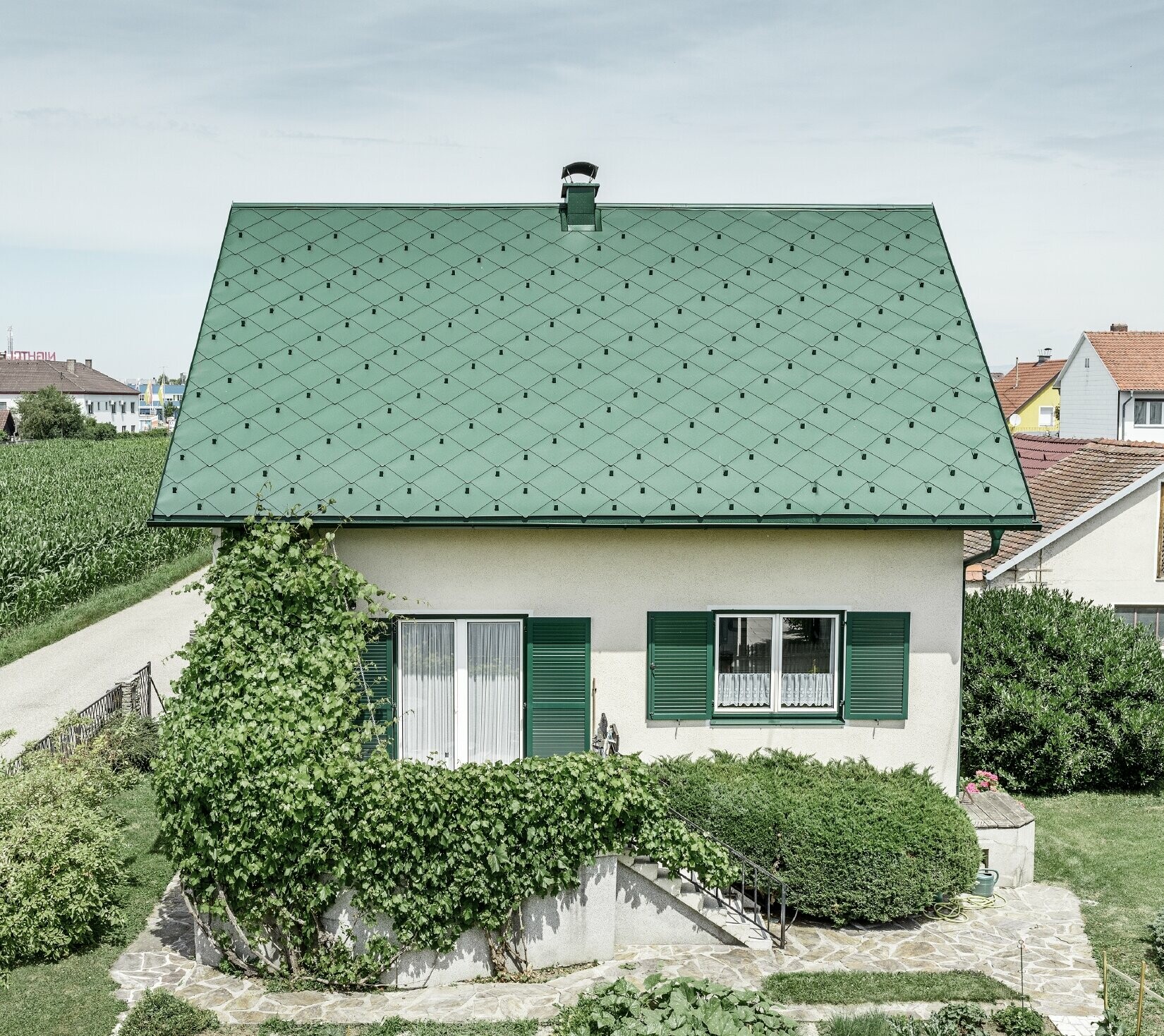 Klassisk enfamilieshus med sadeltag med en taginddækning af aluminium fra mosgrøn med grønne vinduesskodder. Taget blev beklædt med PREFA-tagrombe 44 × 44 i P.10 mosgrøn.
