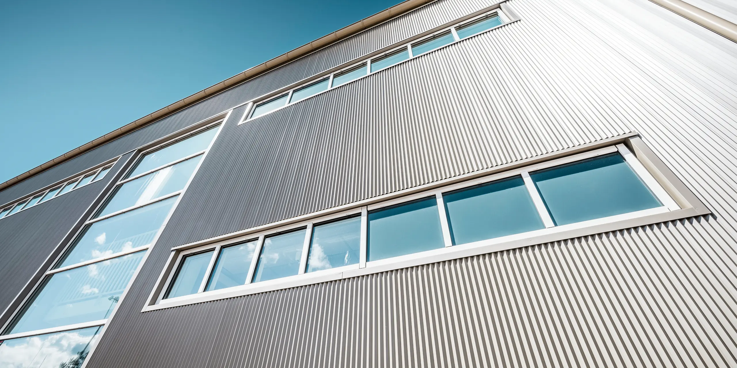 Udvendig udsigt af Park Arena i Värnamo, Sverige, med en moderne PREFA-facade i bronze. De takkede profiler i aluminium skaber markante lys- og skyggeeffekter. De indbyggede vinduer passer harmonisk ind i den præcist bearbejdede facade, der står for lang levetid, modstandsdygtighed og moderne design.