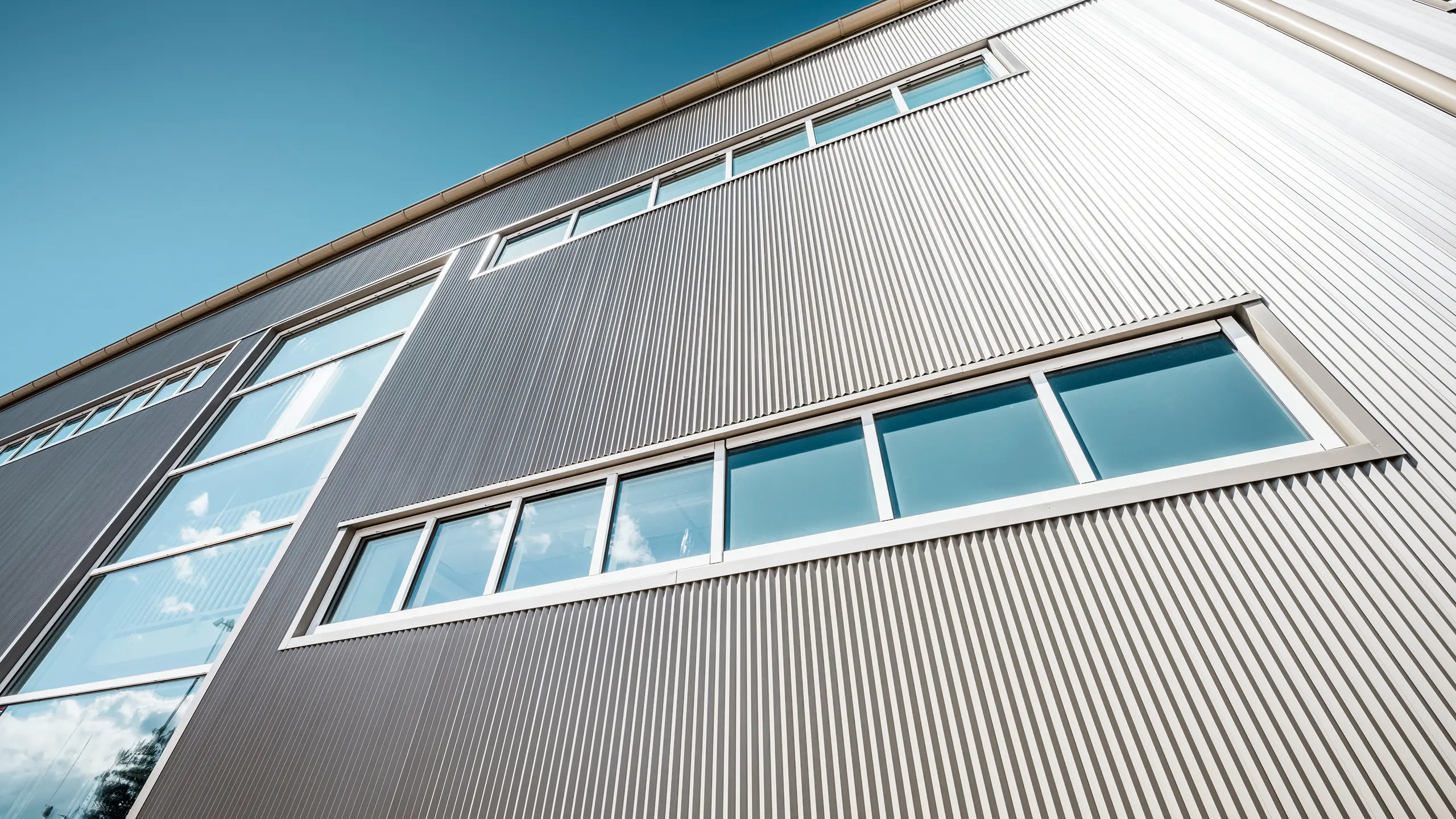 Udvendig udsigt af Park Arena i Värnamo, Sverige, med en moderne PREFA-facade i bronze. De takkede profiler i aluminium skaber markante lys- og skyggeeffekter. De indbyggede vinduer passer harmonisk ind i den præcist bearbejdede facade, der står for lang levetid, modstandsdygtighed og moderne design.