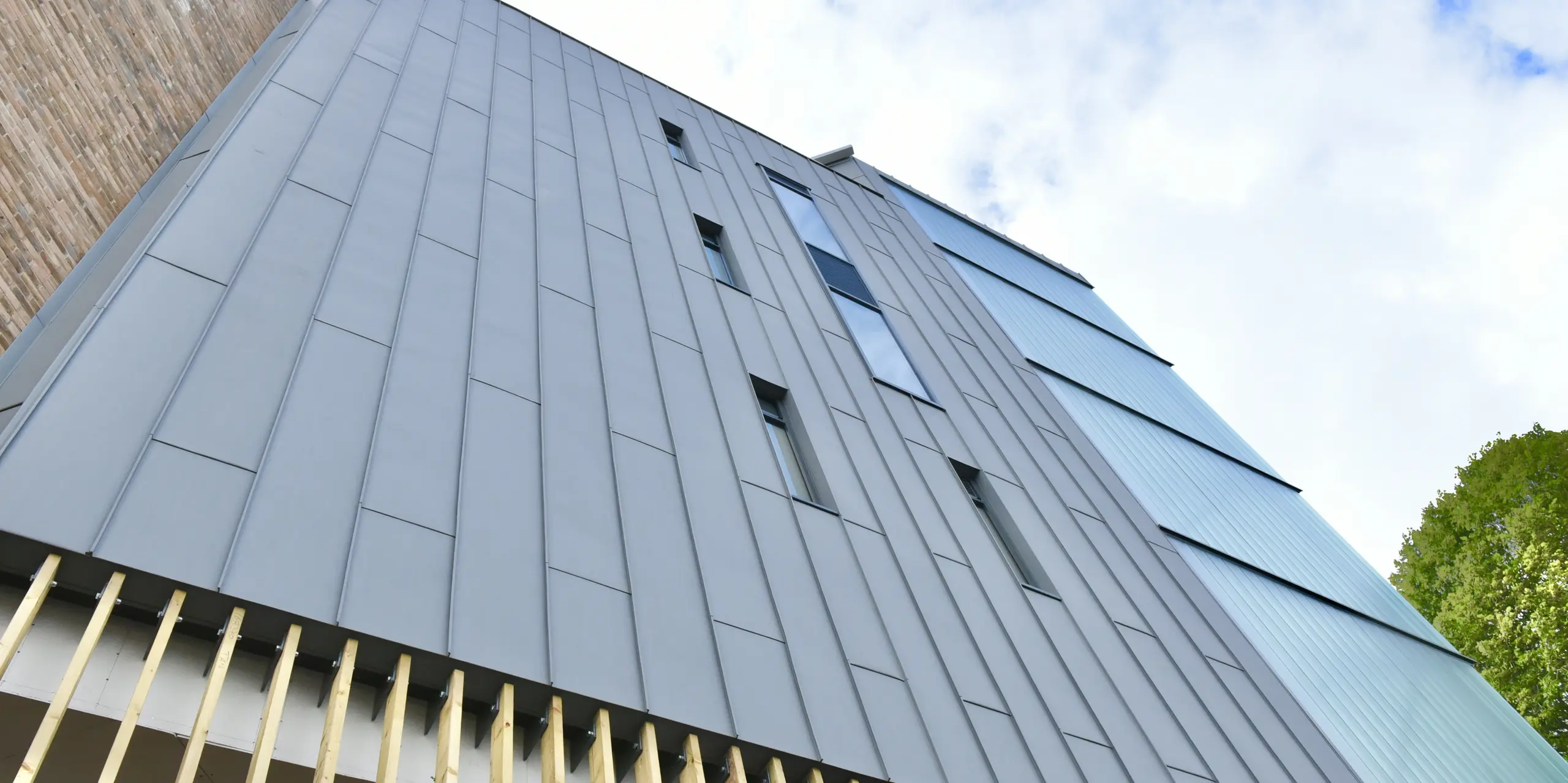 Detailansicht der PREFALZ Stehfalzverkleidung in Patinagrau am North Regional College. Die präzise Verarbeitung des Aluminiums unterstreicht den nachhaltigen und modernen Charakter der Fassade, die sich harmonisch in die Gesamtarchitektur einfügt.