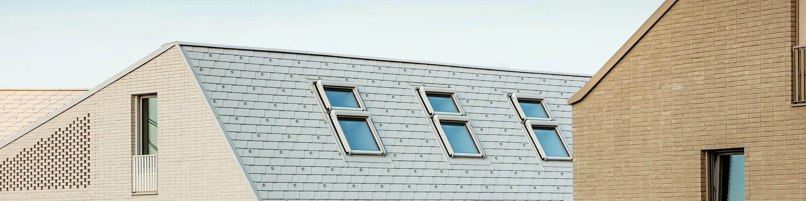 Markante Dachlandschaft im neuen Stadtquartier Vydrica in Bratislava: Steil geneigte Dächer mit präzise verlegten PREFA Aluminium Dachschindeln in P.10 Prefaweiß setzen mit ihren klaren Linien und rhythmisch angeordneten Dachfenstern eindrucksvolle Akzente. Die homogene Oberfläche verbindet Dach und Fassade zu einer eleganten Einheit und greift die ruhige Formsprache der Altstadt auf. PREFA Aluminium überzeugt dabei durch geringes Gewicht, hohe Stabilität, extreme Witterungsbeständigkeit und langlebige, wartungsarme Qualität – ideal für komplexe, architektonisch anspruchsvolle Dachlösungen.