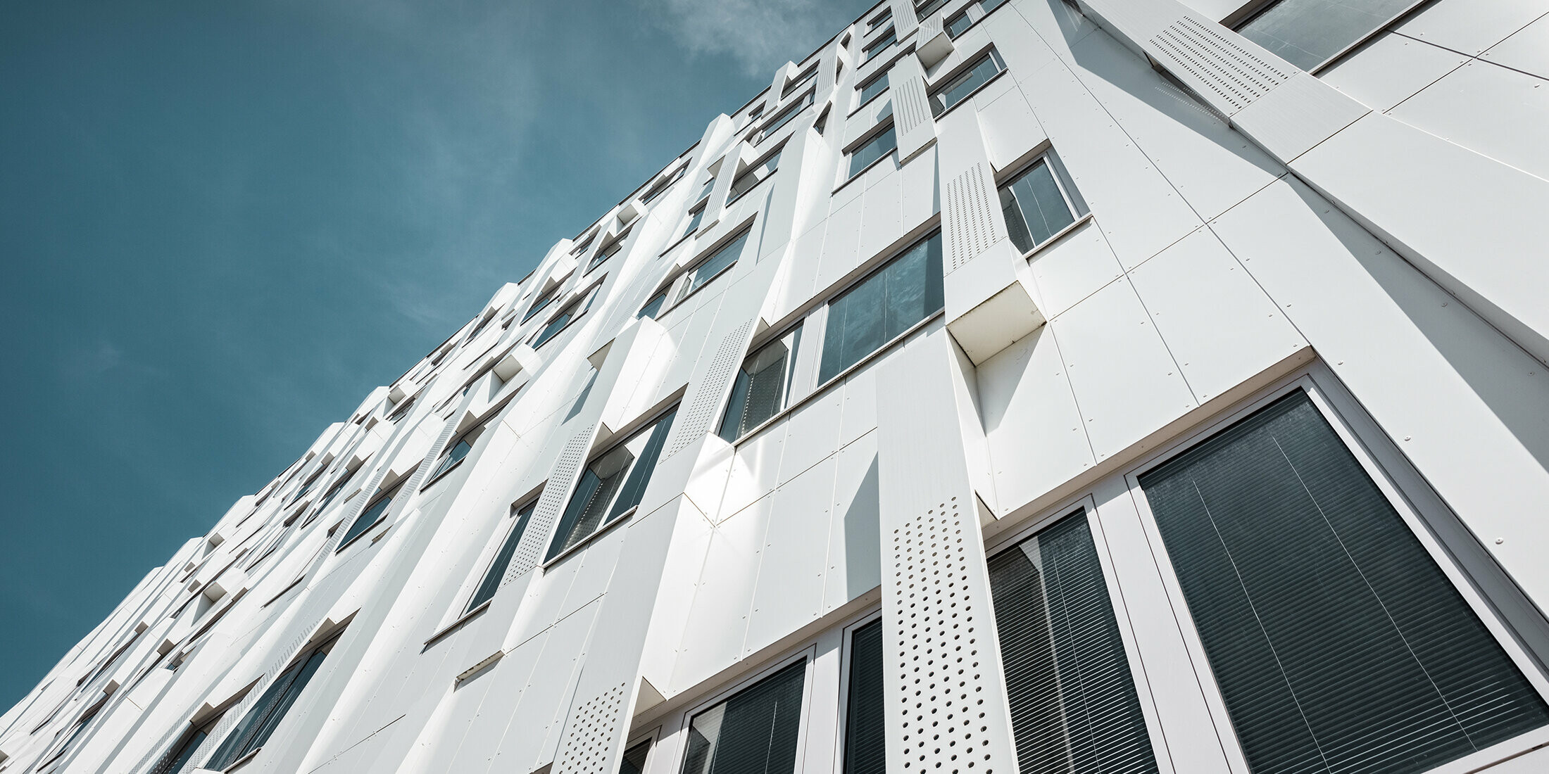 Nahaufnahme der 3D-Fassade mit gelochten Aluminium Verbundplatten-Kassetten und normalen PREFA Verbundplatten in Reinweiß. Die Kassettenfassade von PREFA macht das Gebäude zu einem Blickfang.