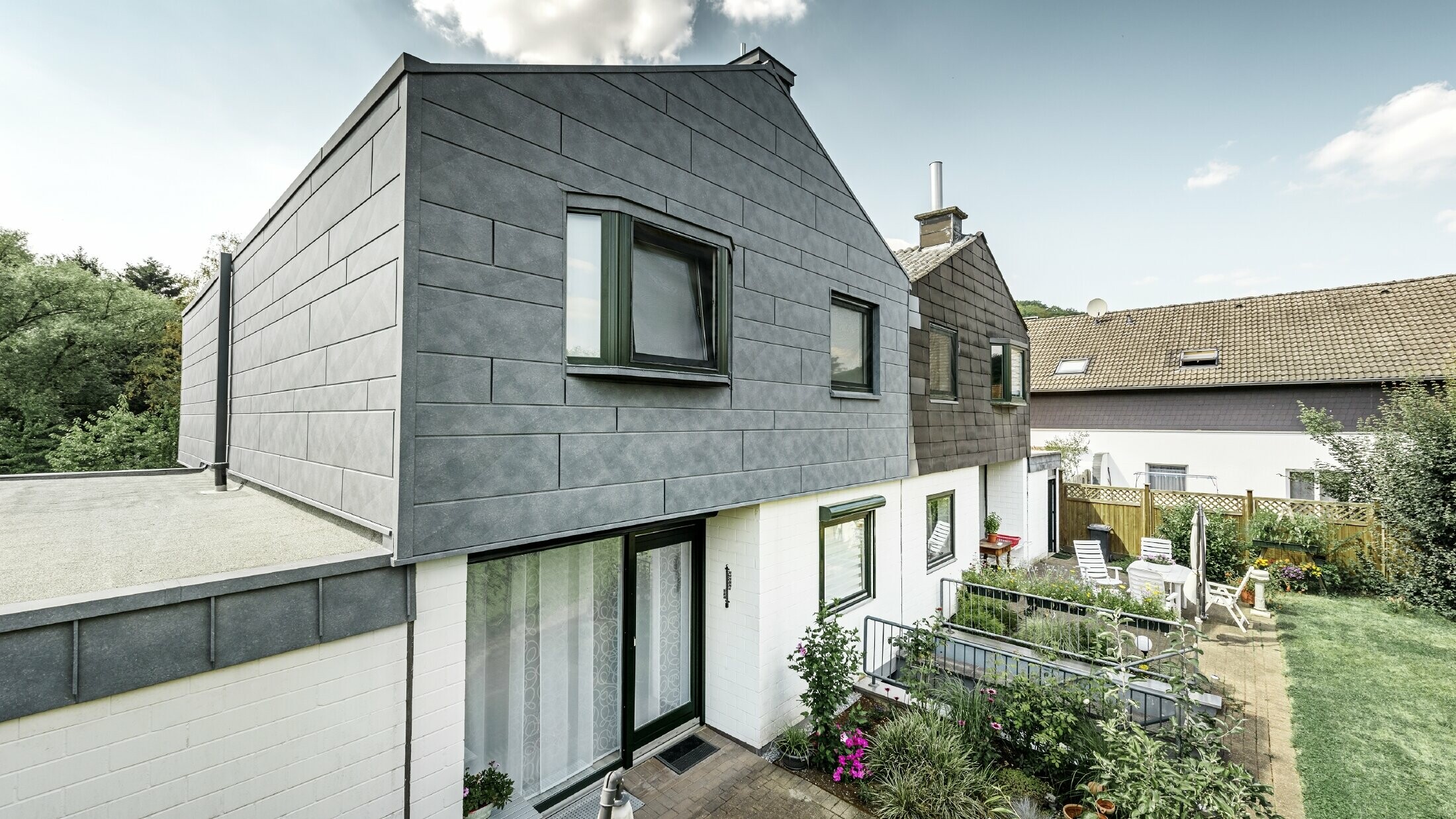 Den øverste del af bygningen på den ene halvdel af dobbelthuset er renoveret med PREFA-facadeelementet Siding.X i P.10 stengrå. Ved siden af ser man halvdelen af huset før renoveringen til sammenligning.