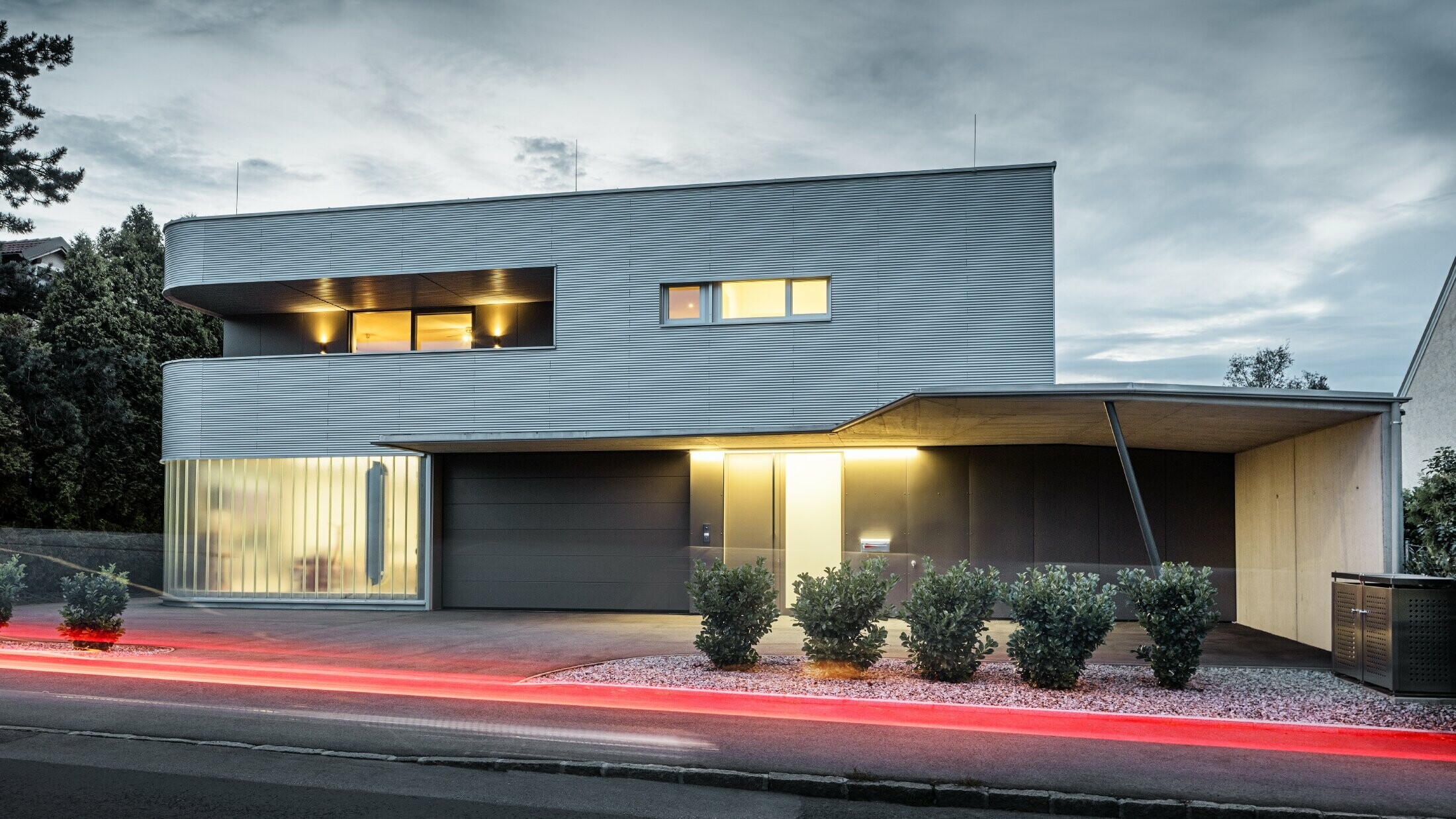 Moderne bolighus med naturblank facade af PREFA-profilbølge med garage fotograferet i aftenlys