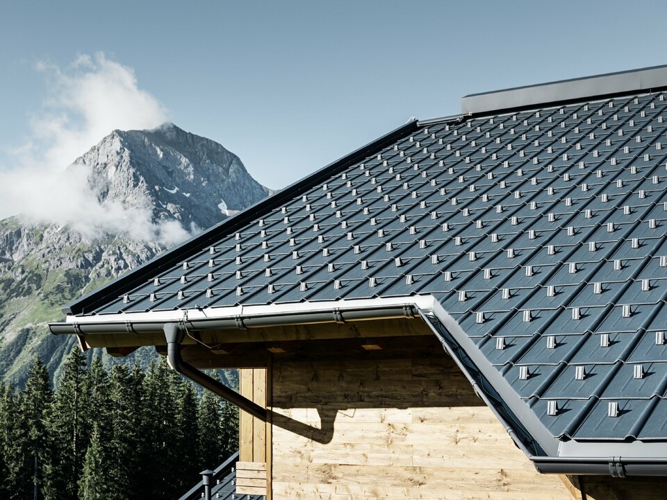 Holzhaus in den Bergen, das Dach ist eingedeckt mit der PREFA Dachplatte in Anthrazit mit PREFA Dachrinne und Holzfassade