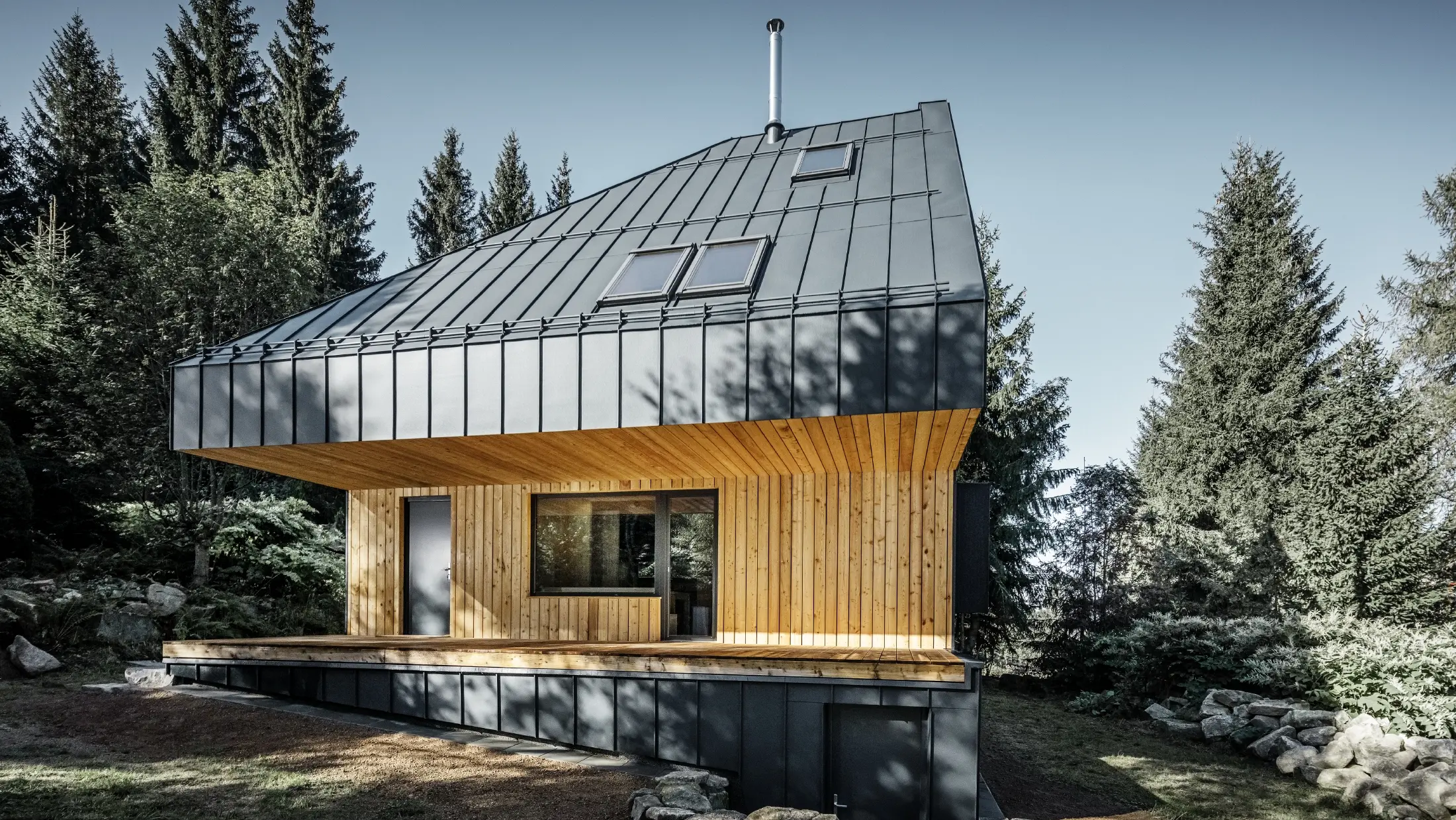 Arkitektonisk parcelhus i skoven, det imponerende tag blev beklædt med PREFA Prefalz aluminium i antracit. Undertaget og facaden er beklædt med træpaneler.