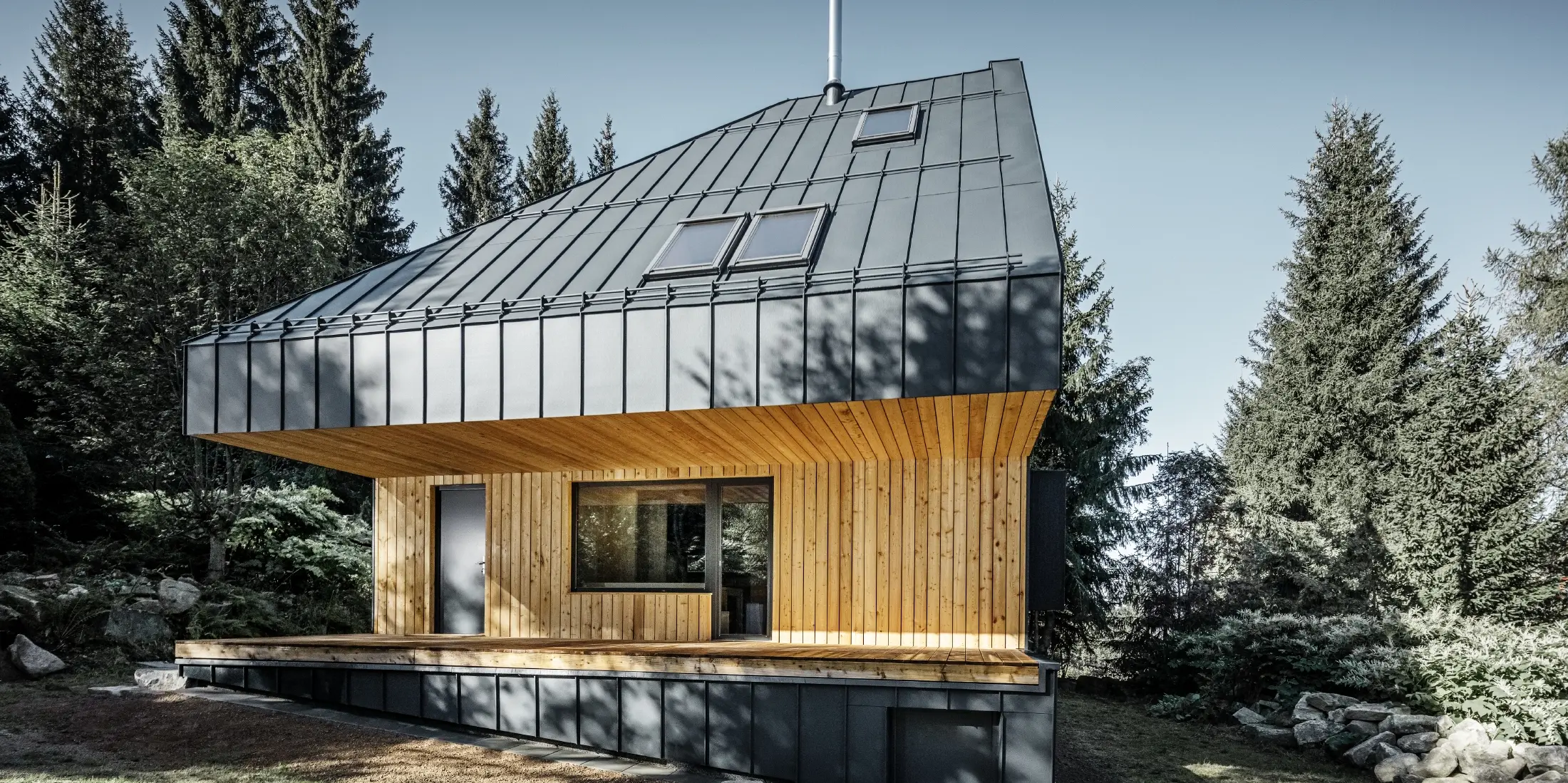 Arkitektonisk parcelhus i skoven, det imponerende tag blev beklædt med PREFA Prefalz aluminium i antracit. Undertaget og facaden er beklædt med træpaneler.