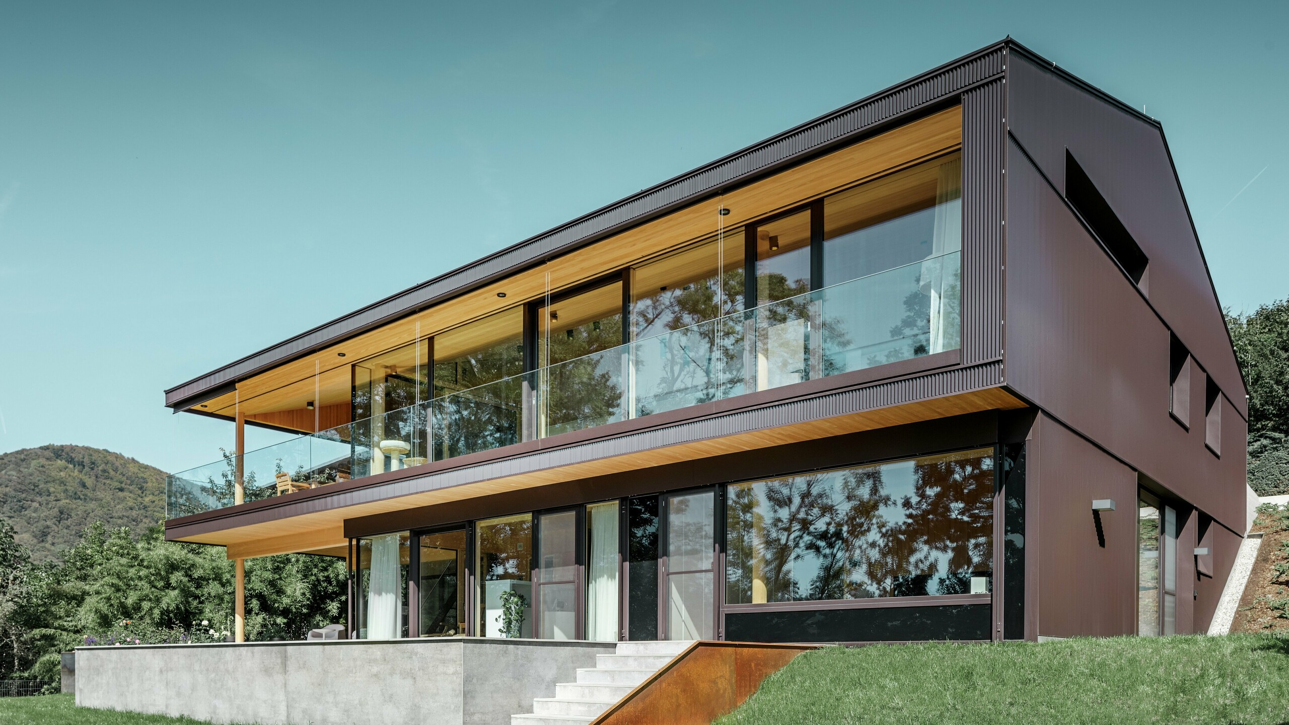 Dette moderne enfamilieshus befinder sig midt i naturen. Bygningens facade blev beklædt med PREFA-takker i farven nøddebrun. Beklædningen passer derved både til huset og til det omliggende landskab.