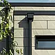 Moderne parcelhus med fladt tag og smalle vinduer. Facaden er beklædt med PREFA Siding.X-facade med rynket udseende i farven bronze. Forbindelserne blev lavet i antracit. PREFA-kvadratrør med tilhørende vandopsamlingsbeholder i antracit bruges til tagafvanding.