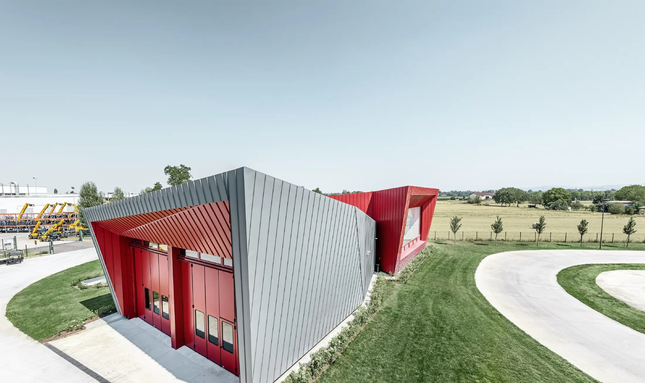 Moderne træningscenter fra Dieci i Montecchio Emilia , Italien, med tribune med aluminiumfacade med Prefalz i lysegrå og Falzonal i karminrød