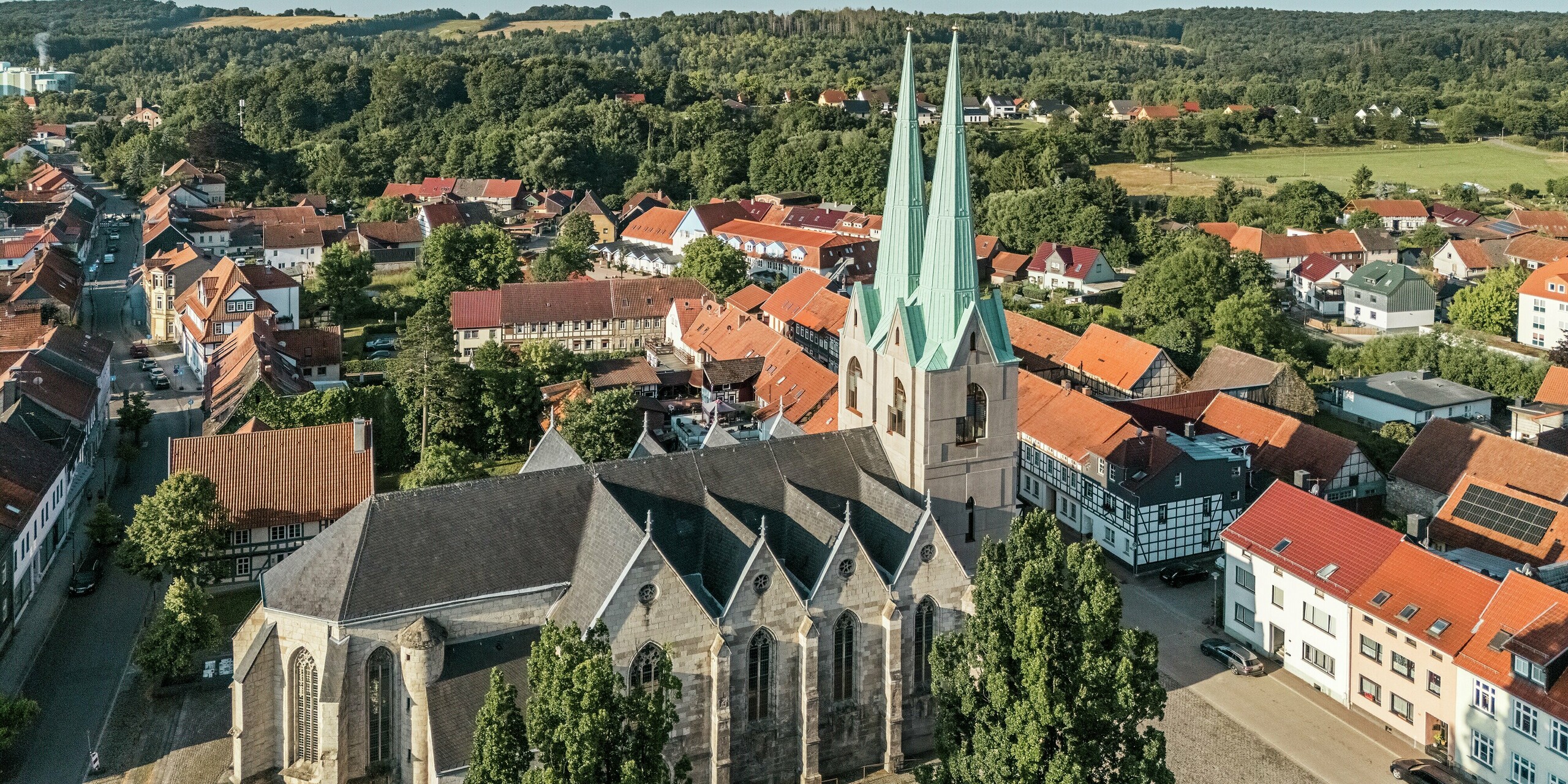Weitwinkel-Drohnenaufnahme der Stadtkirche St. Johannis in Ellrich, eingebettet in das historische Stadtbild. Besonders hervorstechend: die neu errichteten Turmspitzen mit PREFALZ in P.10 Patinagrün, die sich elegant vom traditionellen Umfeld abheben. Das witterungsbeständige Aluminiumdach vereint moderne Technik mit denkmalgerechter Gestaltung – ein echtes Highlight im Stadtzentrum.