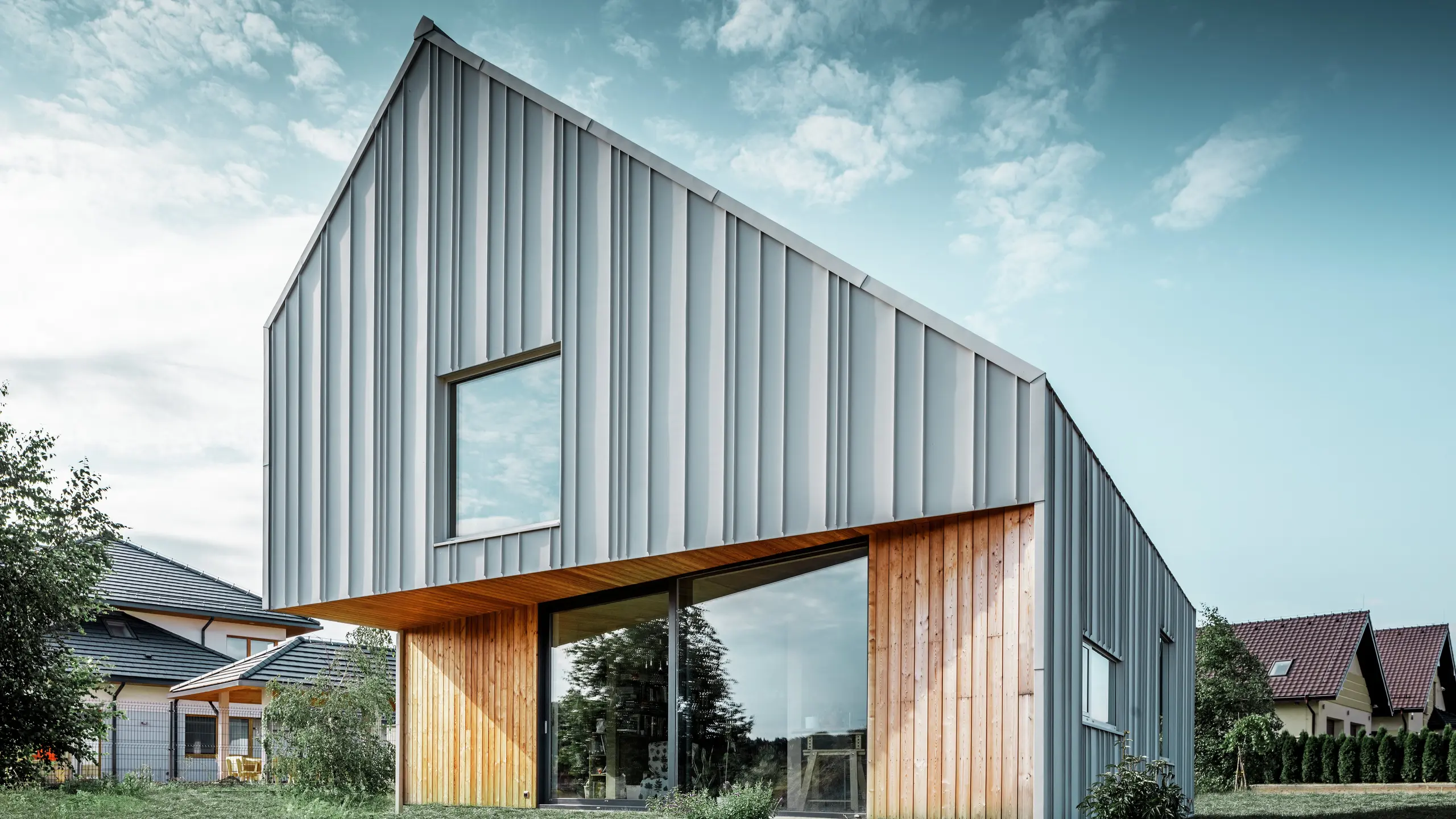 Moderne parcelhus med skråt tag uden udhæng og aluminiumsfacade fra PREFA i hvid. En træfacade er kombineret med lodrette træpaneler i stueetagen. 