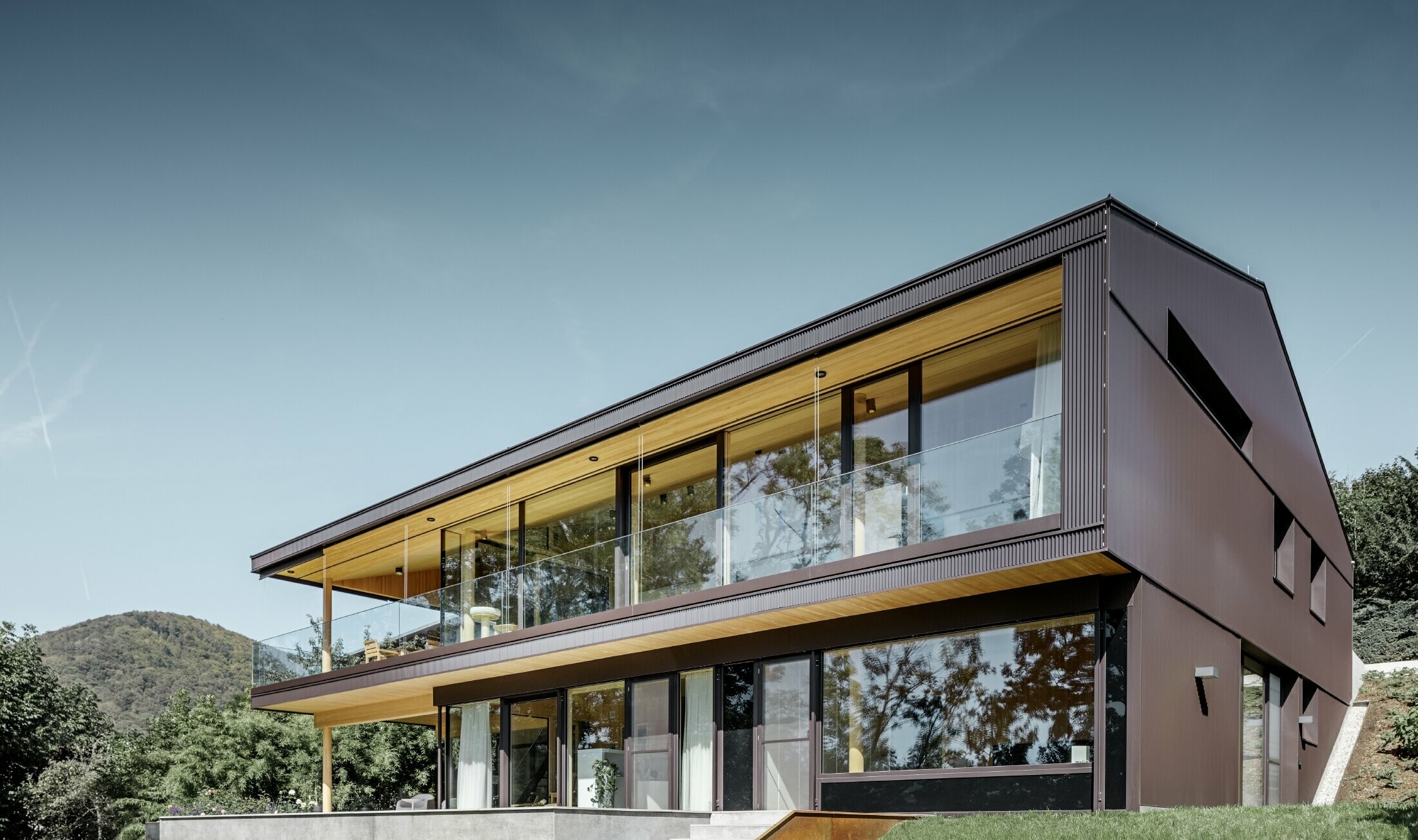 Moderne enfamilieshus med store vinduer set fra havesiden, facaden er beklædt med PREFAs takkede profil i mørkebrun.