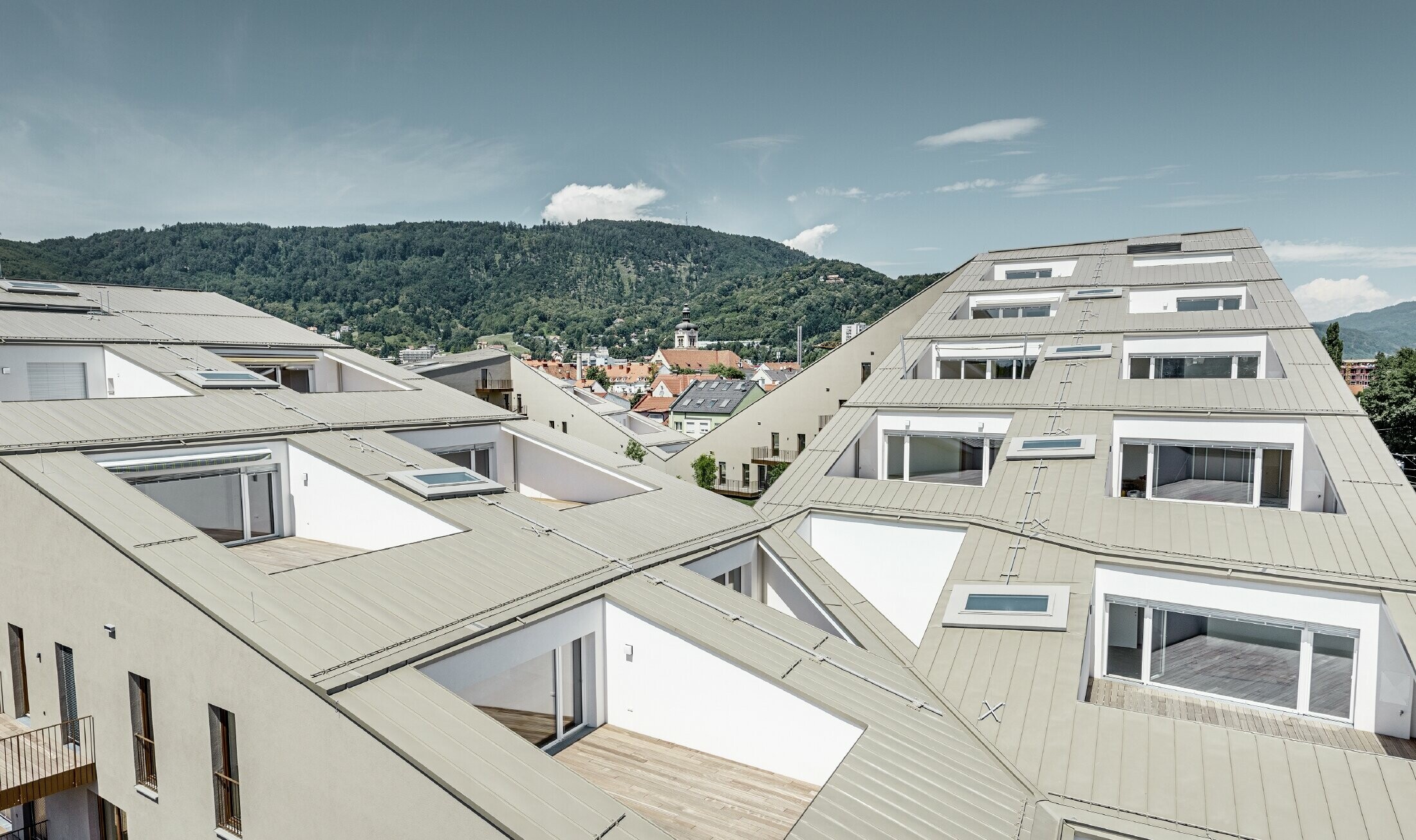 Langt boliganlæg i Graz med flade tagflader og integrerede terrasser og udstrakte vinduer med et Prefalztag i specialfarven bronzemetallic