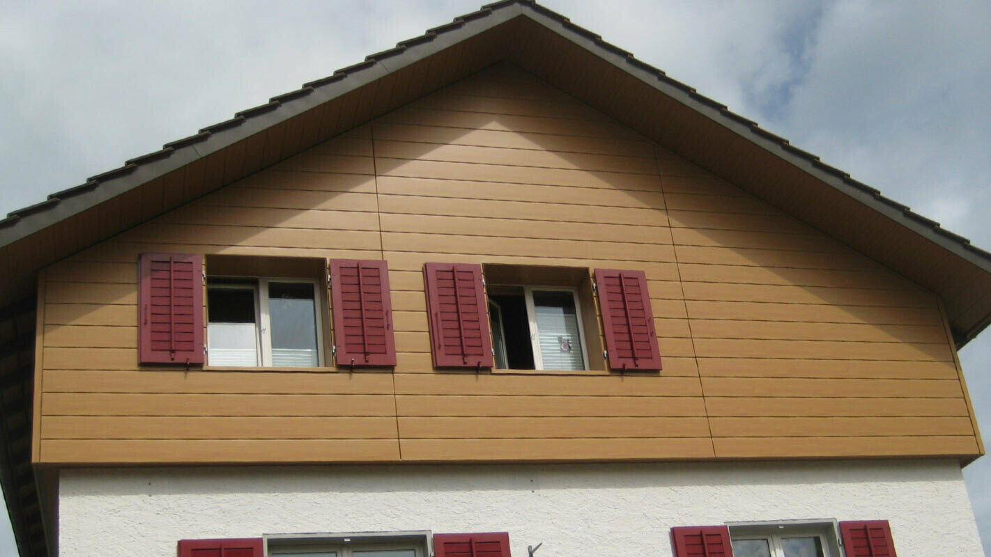 Husfacade i trælook med vandrette PREFA sidings, vinduer med røde skodder