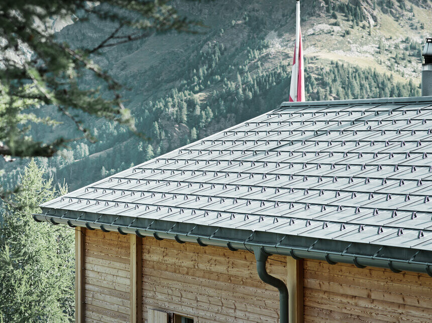 Schweisisk hytte beklædt med PREFA-tagplade og hængende PREFA-tagrende, der er fastgjort med overbøjler.