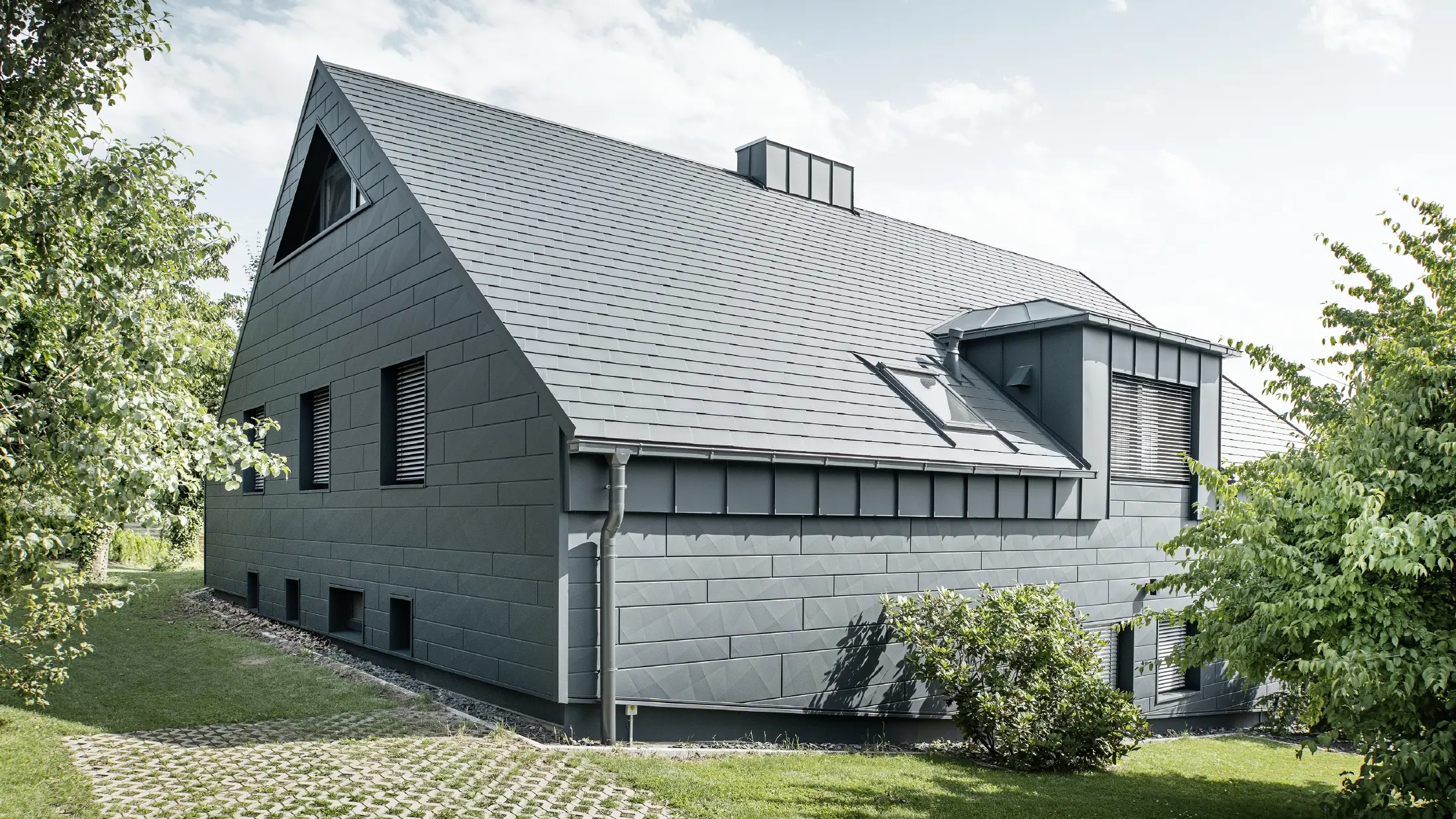 Stort enfamiliehus med sadeltag og mange vinduer. Hele huset er beklædt med en aluminiumsbeklædning i antracit, på taget er der anvendt PREFA aluminiums tagspån, og på facaden er der anvendt Siding.X i antracit.