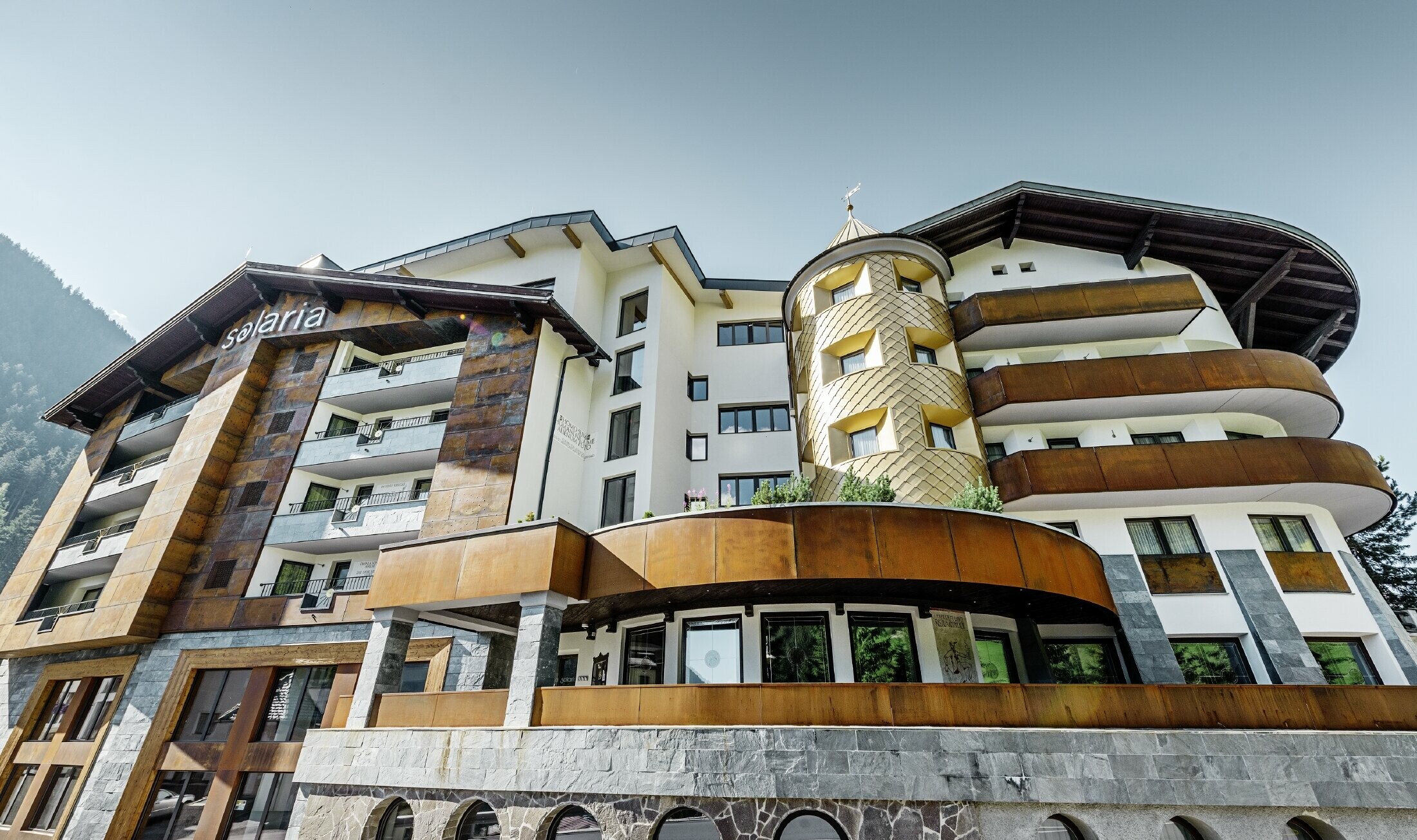 Traditionelt hotel i Ischgl med træbalkoner og træfacade og et tårn med gyldne alu-tagromber fra PREFA