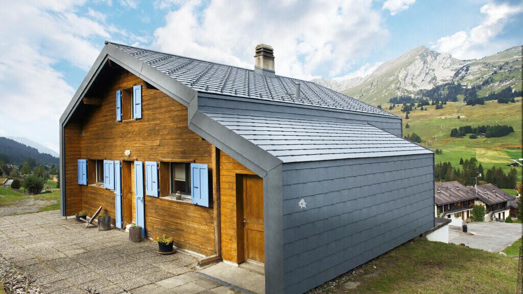 Hus i bjergene i Schweiz med træfacade kombineret med PREFA-tagrombe og -vægrombe i stengrå