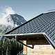 PREFA-tagplade i alpin anvendelse – tagplade i antracit opsat på hytte i Lech am Arlberg med bjerge i baggrunden; PREFA-tagrende i antracit; træfacade