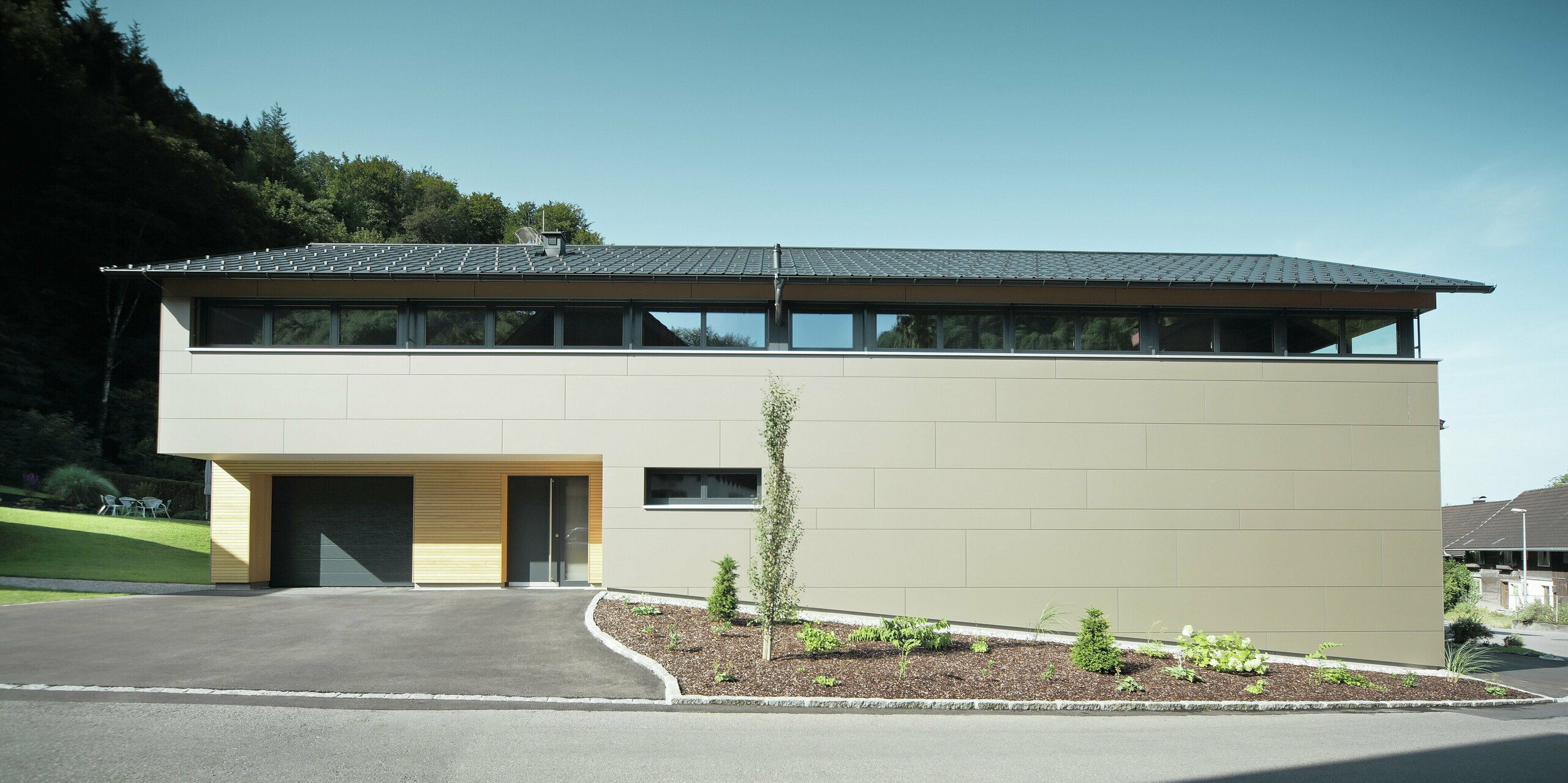 Langhus med PREFA tagpanel i P.10 antracit, kombineret med PREFA kompositpanel i bronze på facaden; moderne byggestil kombineret med smalle vinduer og træfacade