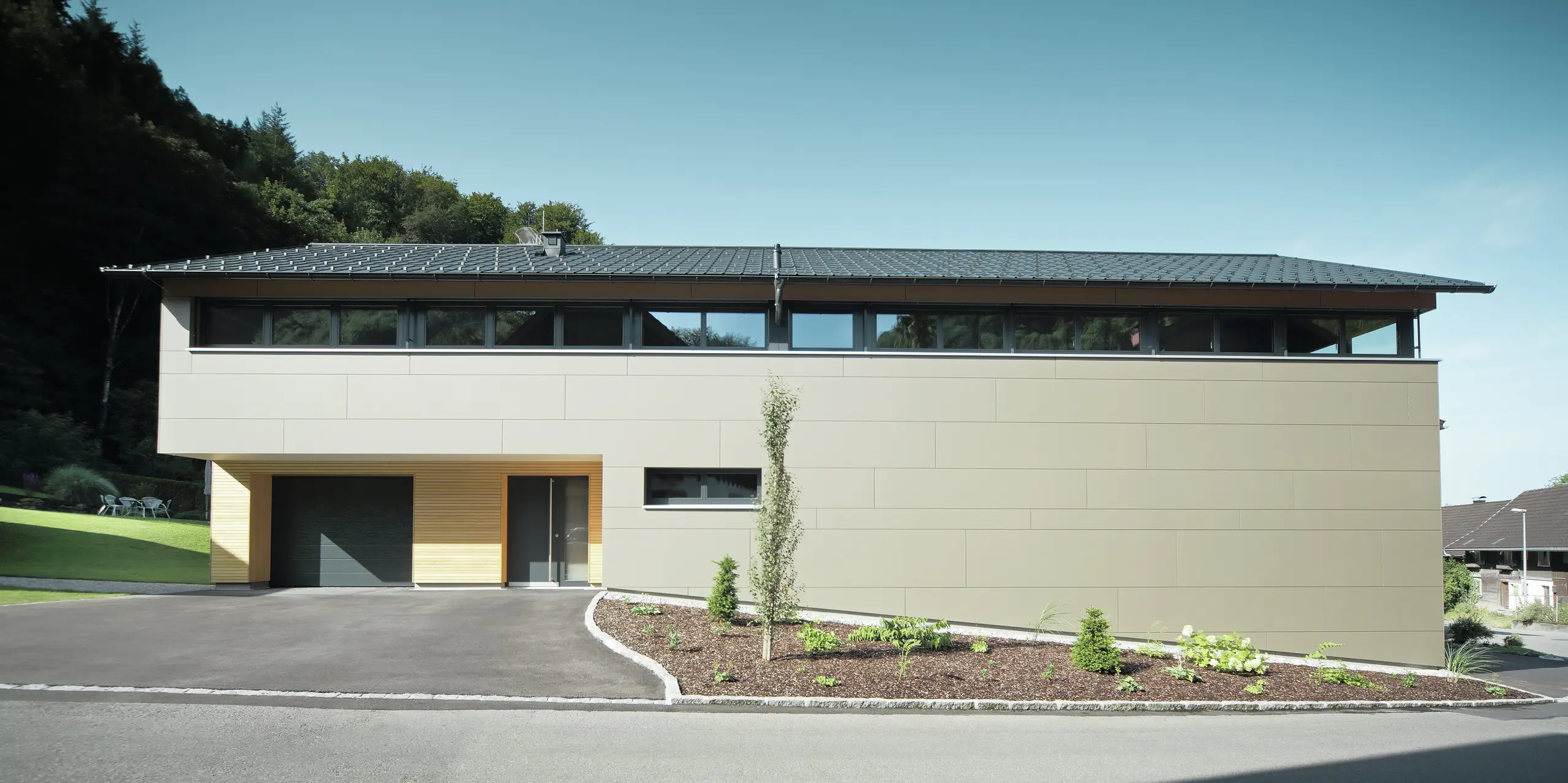 Langhus med PREFA tagpanel i P.10 antracit, kombineret med PREFA kompositpanel i bronze på facaden; moderne byggestil kombineret med smalle vinduer og træfacade