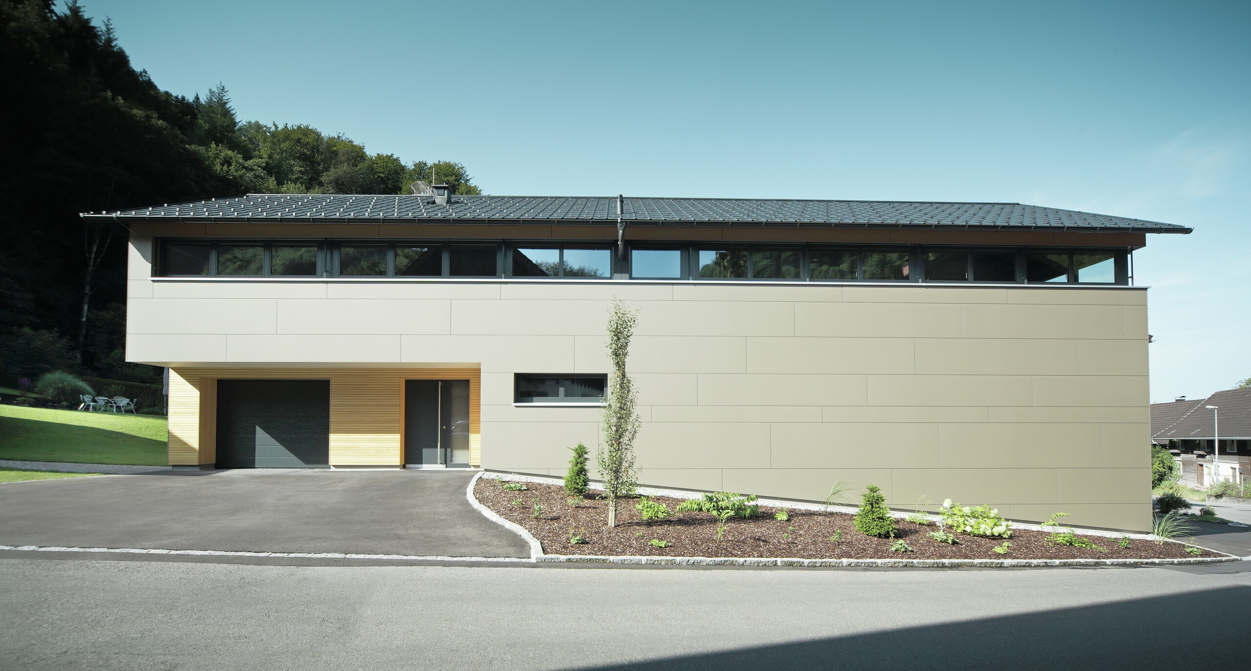 Langhus med PREFA tagpanel i P.10 antracit, kombineret med PREFA kompositpanel i bronze på facaden; moderne byggestil kombineret med smalle vinduer og træfacade