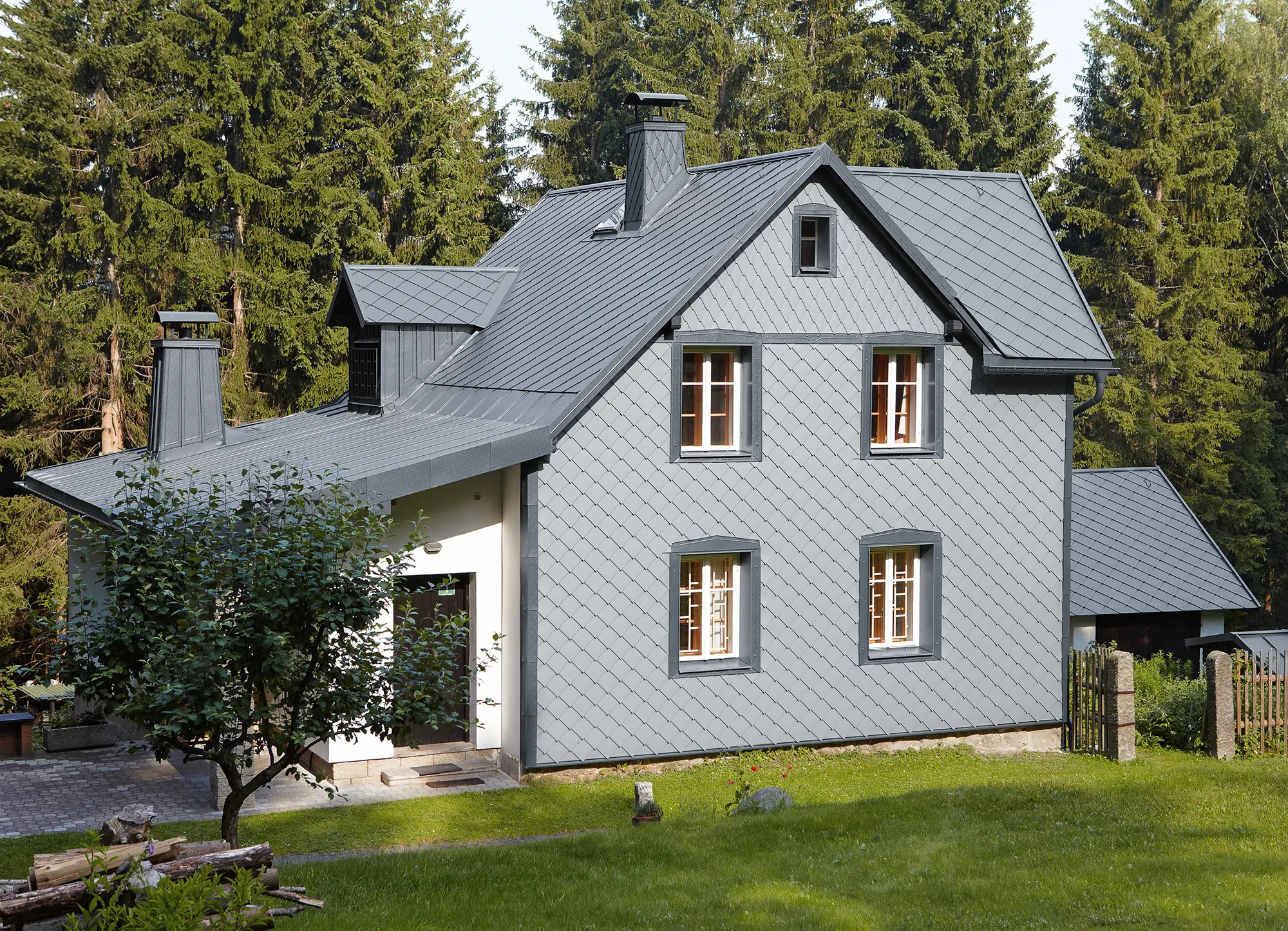 Enfamilieshus i skovområde med vejrbestandig PREFA-aluminiumsfacade i lys grå.