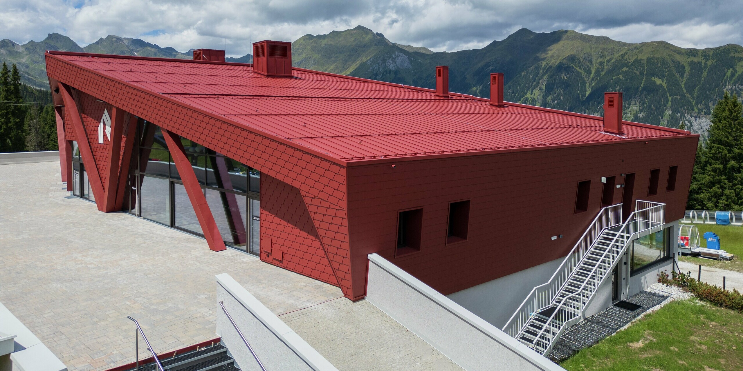 Die beeindruckende Architektur des Summit Mountain Clubs in Ratschings zeigt das markante P.10 Oxydrot am Dach und der Fassade. Die moderne Formensprache und die kräftige Farbgestaltung in Rot bilden einen starken Kontrast zur grünen Berglandschaft. Besonders hervorzuheben sind die großen Fensterflächen und das innovative Dachdesign, das nicht nur ästhetisch beeindruckt, sondern auch funktional und robust ist – ideal für das alpine Klima.