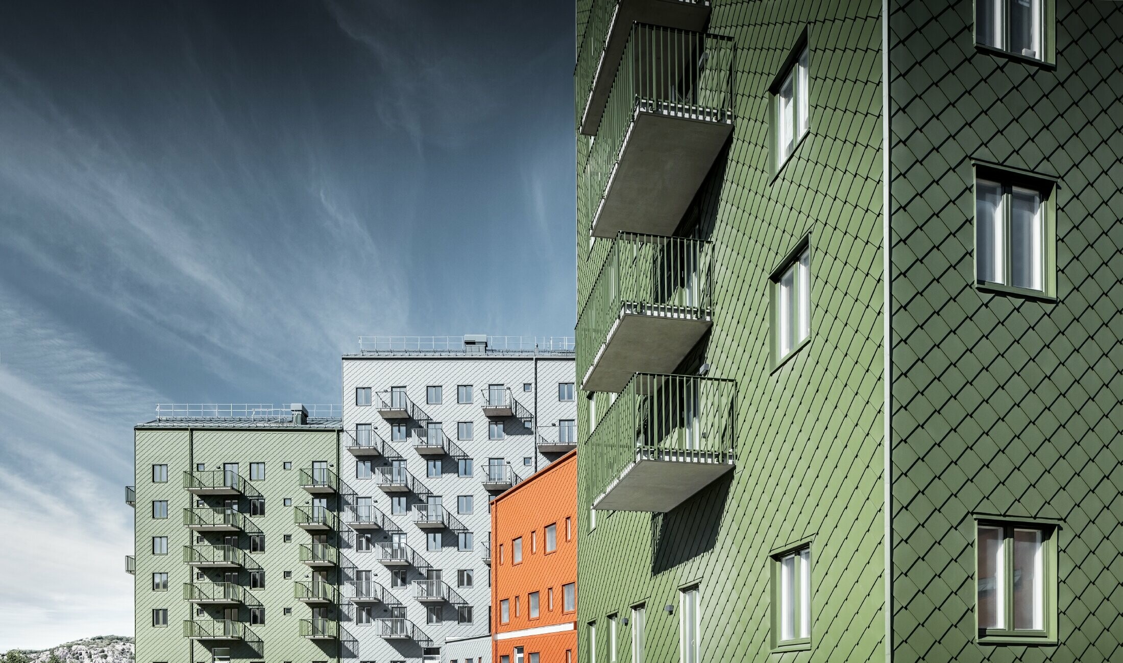 Flere beboelsesejendomme ved siden af hinanden, beklædt med PREFA-vægrombe 29 × 29 i farverne murstensrød, olivengrøn og lysegrå.