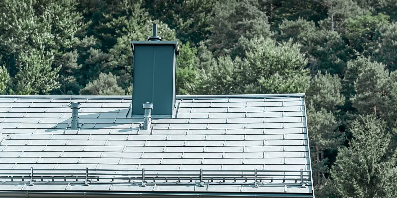 Detaljeret visning af et sadeltag, belagt med den stengrå PREFA tagplade R.16 med snefangssystem, skorstensinddækning, tagrende og udluftningsrør, ligeledes fra PREFA