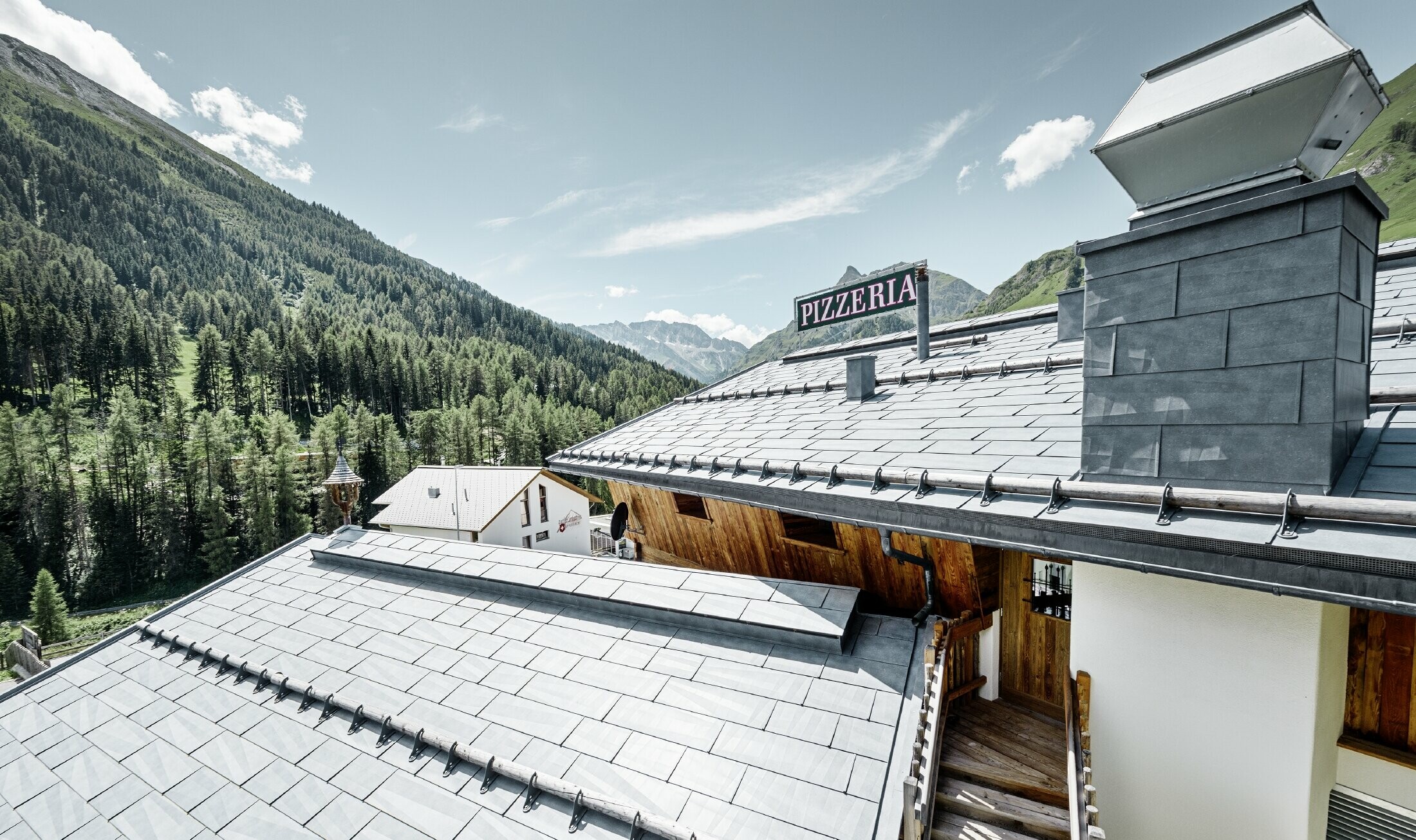 Restaurant Almrausch med bjerge i baggrunden og et PREFA tag med tagpanel FX.12 in stengrå og bjergsnestøtter