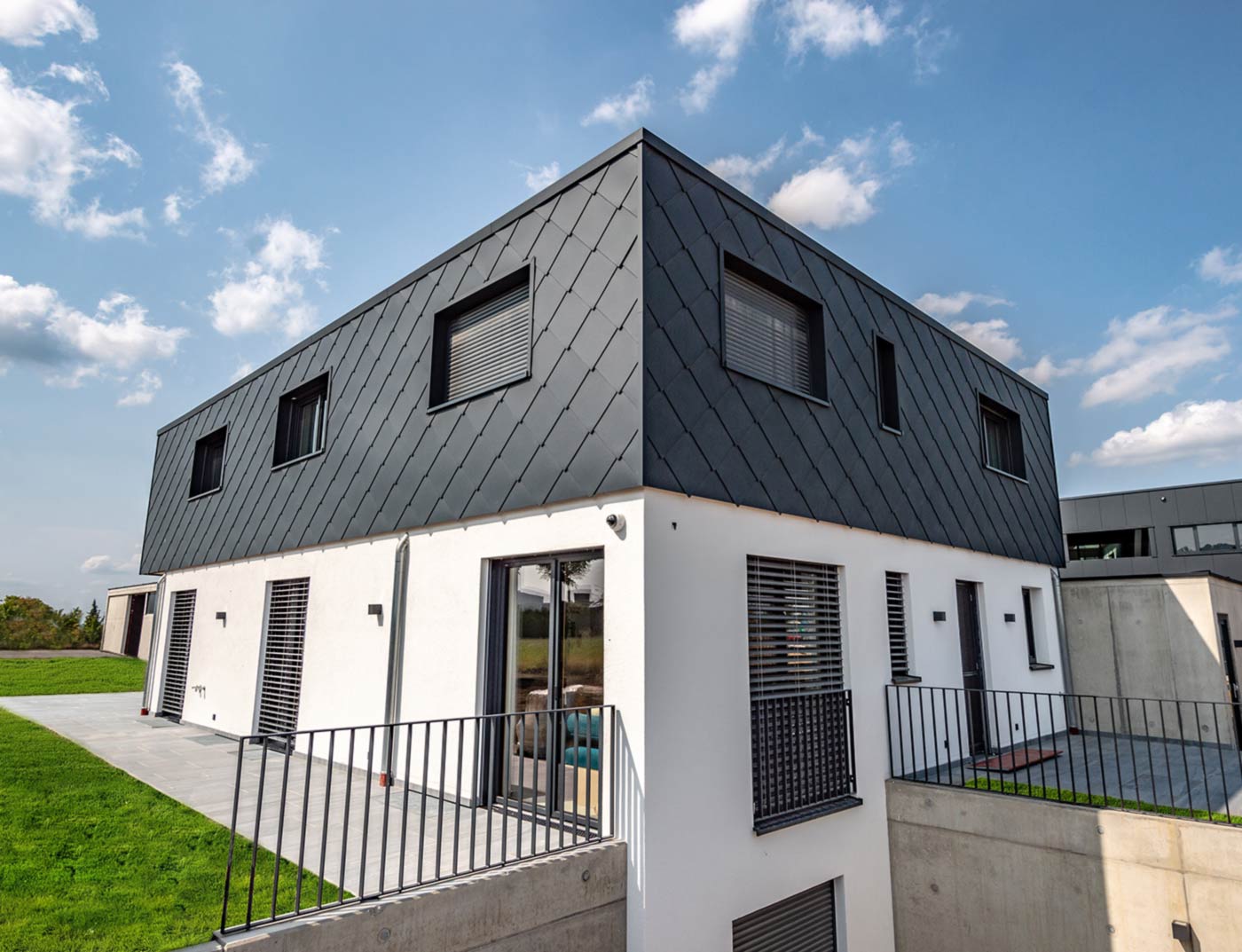 PREFA vægrombe 44 × 44 antracit reference Moderne nybyggeri med fladt tag - facaden på den øverste etage er beklædt med PREFA aluminium vægrombe 44 × 44 i antracit. Den nederste del af facaden er hvid puds.